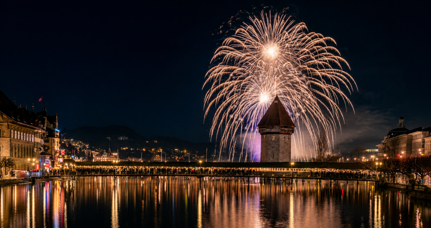 Grosses professionelles Feuerwerk über dem Luzerner Wasserturm an der Kapellbrücke mit Spiegelung im Vierwaldstättersee und zahlreichen Zuschauern am Ufer.