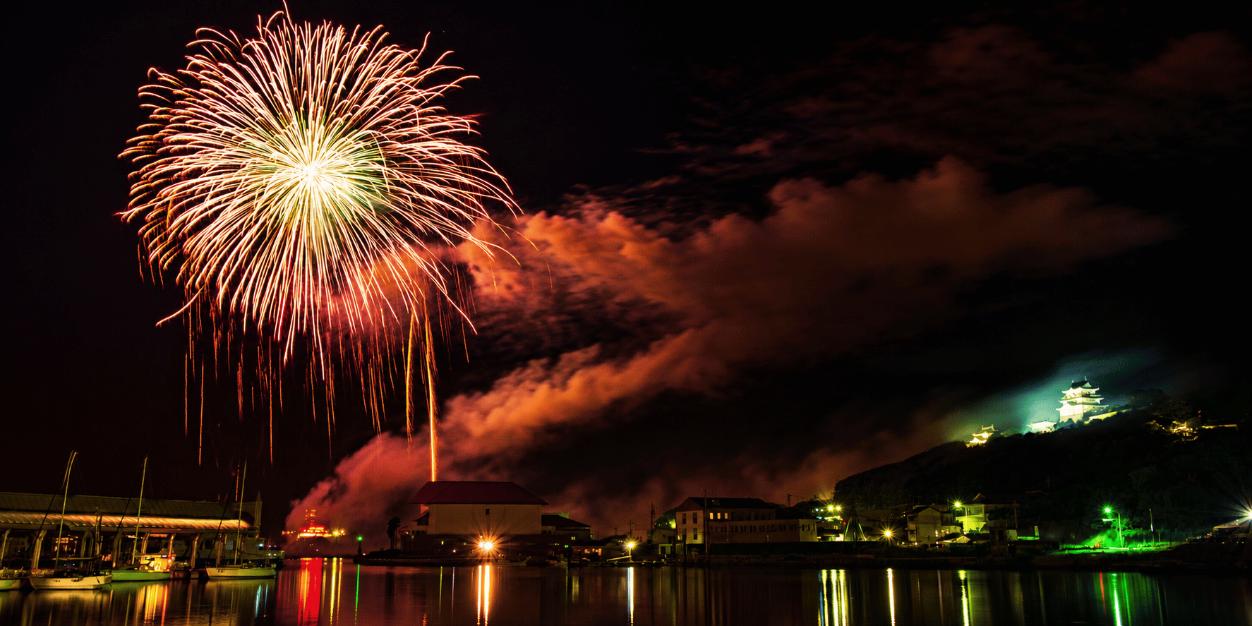 Spektakuläres Grossfeuerwerk des Kamuro Feuerwerksvereins über einem Hafen bei Nacht mit farbenprächtigen Effekten und Spiegelungen auf dem Wasser.