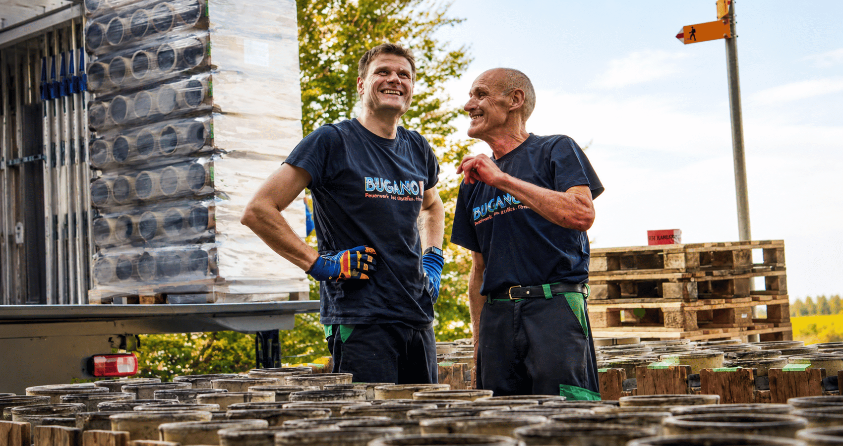 Zwei Mitarbeitende von Bugano beim Verladen von Feuerwerksmaterial auf einem Lagerplatz – Teamarbeit und Vorbereitung einer Feuerwerksveranstaltung.